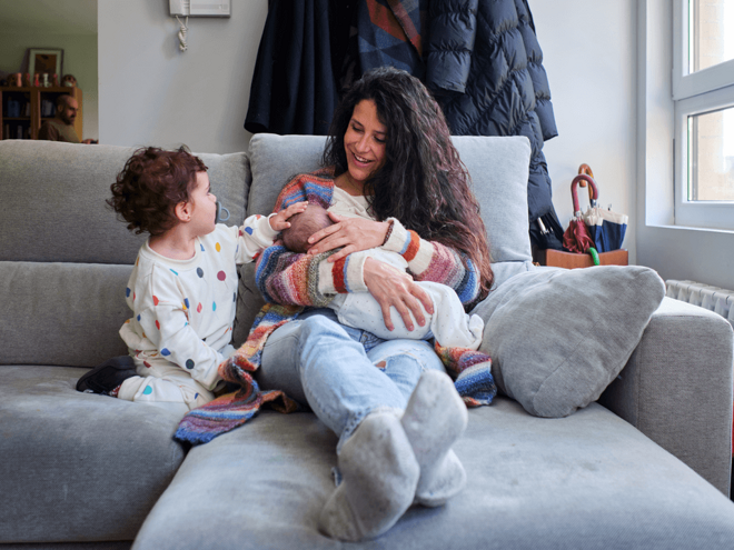 A mom enjoying breastfeeding benefits with her baby alongside her toddler.