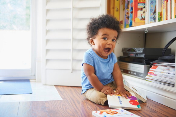 Surprised baby boy sitting on floor playing with books