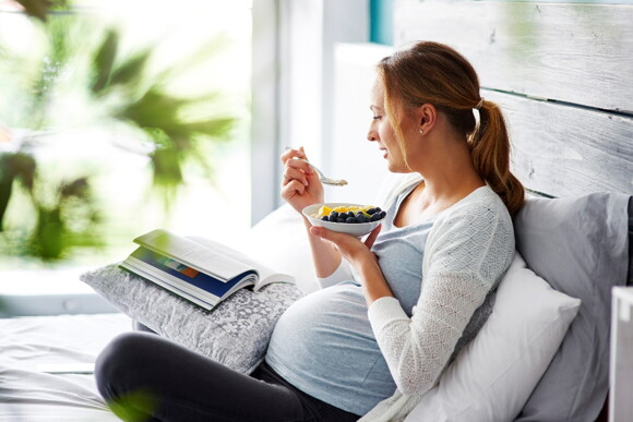 A woman eating fruit on the couch while reading.