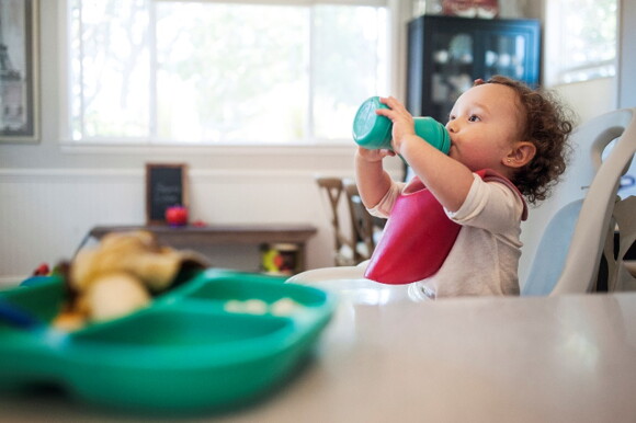 A baby drinking water while sitting in highchair at home.