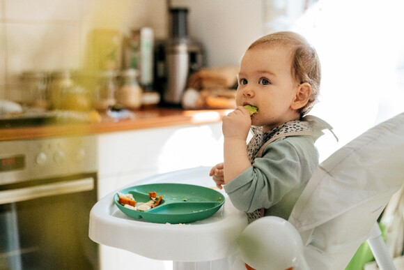 A toddler feeding himself with vegetables.